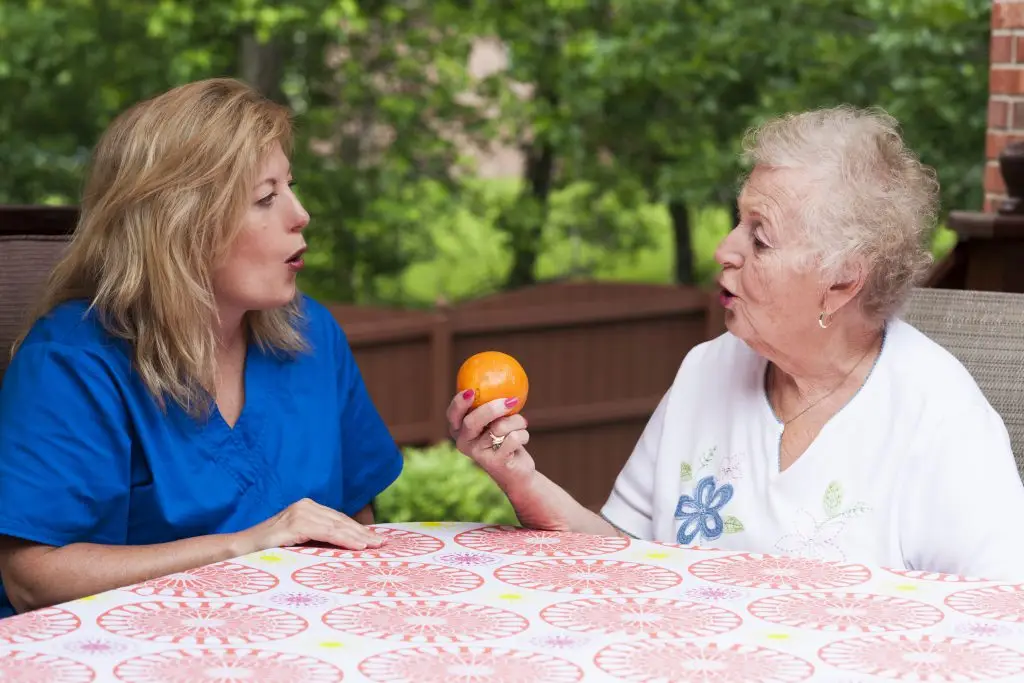 Speech therapist with female stroke patient outdoors during a home health therapy session modeling the production of a consonant during speech training for apraxia