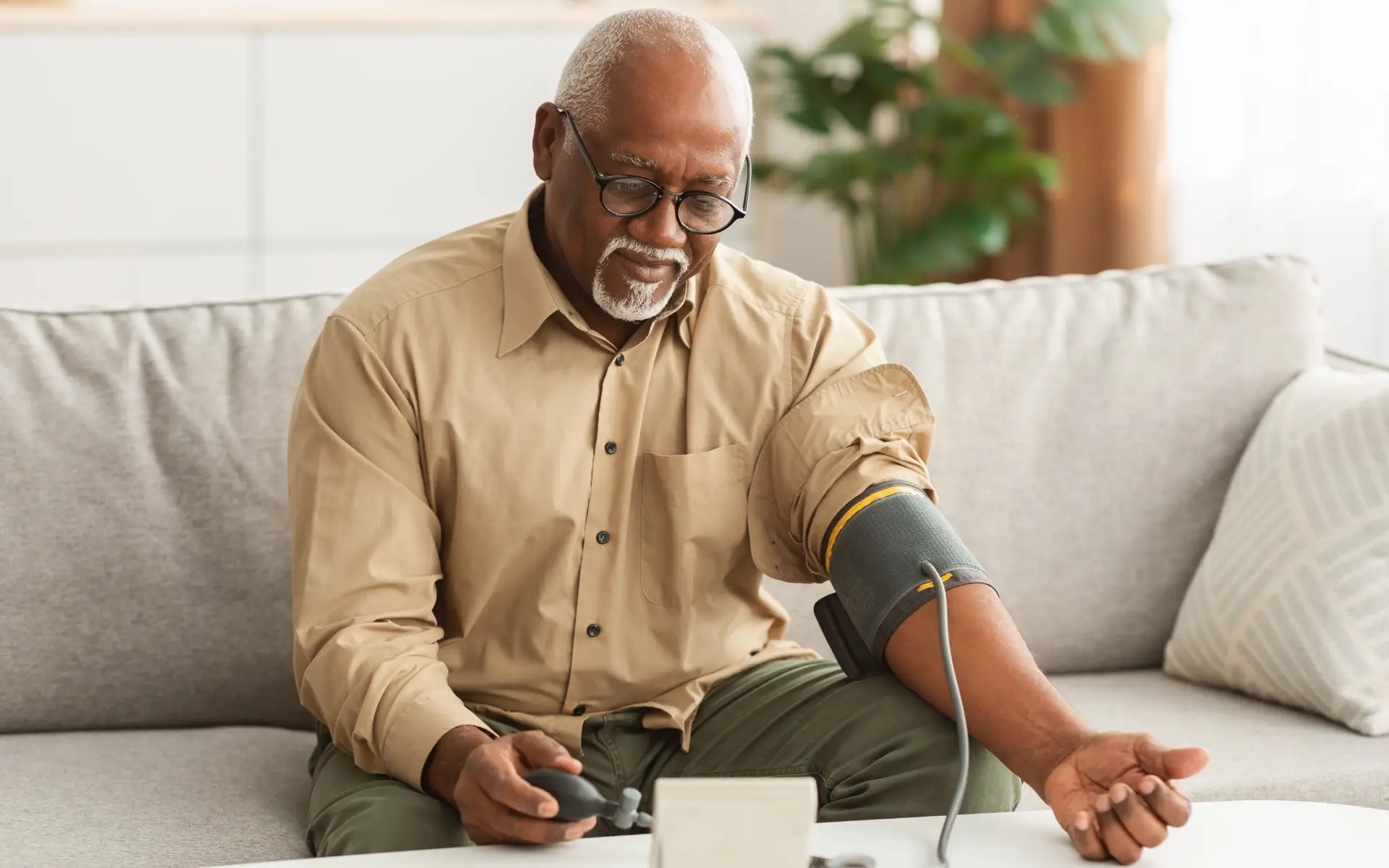 senior african american man sitting on couch taking his blood pressure